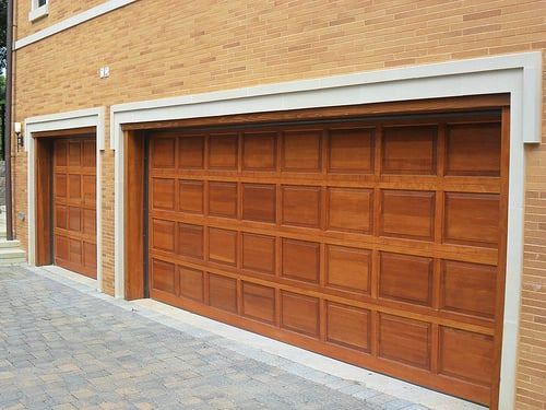 A pair of wooden garage doors on a brick building.