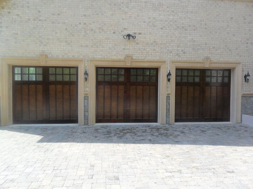 Three wooden garage doors are on a white brick building.