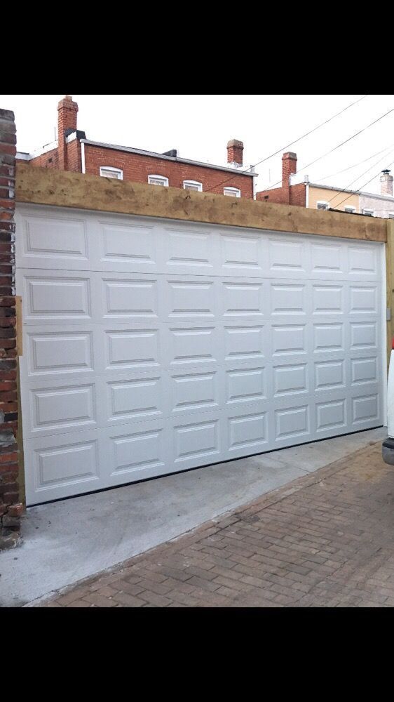A white garage door is sitting in front of a brick building.